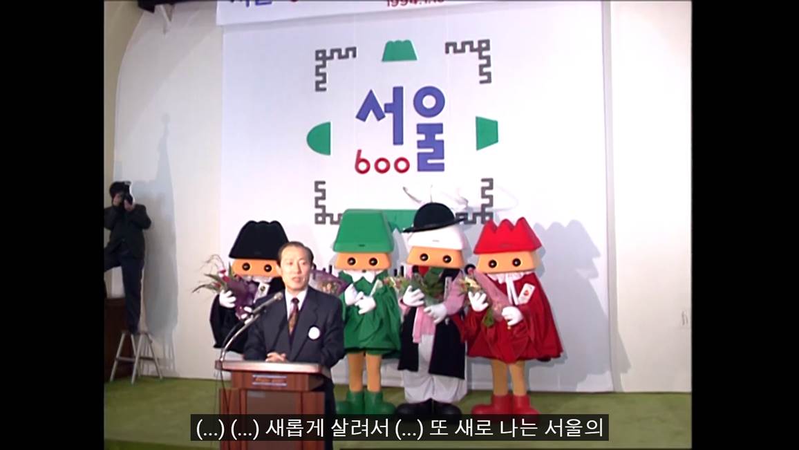 모자와 원피스를 입은 마스코드, 포졸모자를 쓰고 포졸 옷을 입은 마스코트 들이 꽃다발을 들고 서있는 중이다. 서울 600이라고 적힌 포스터를 뒤로하고 관계자가 연설중이다.
